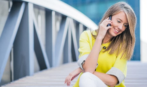 blonde sitting on bridge smiles while talking on phone
