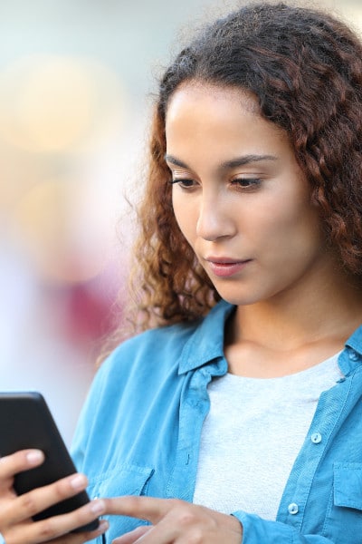 brunette in denim shirt reads cell phone screen