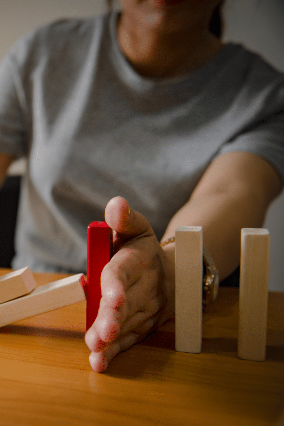 hand of person in gray shirt stops falling dominoes