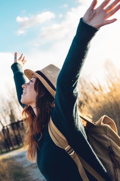 brunette in hat outdoors with arms in air