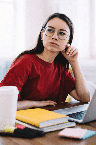 female college student thinking at desk with laptop