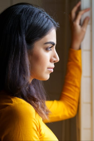 sad young woman in yellow top looks out window