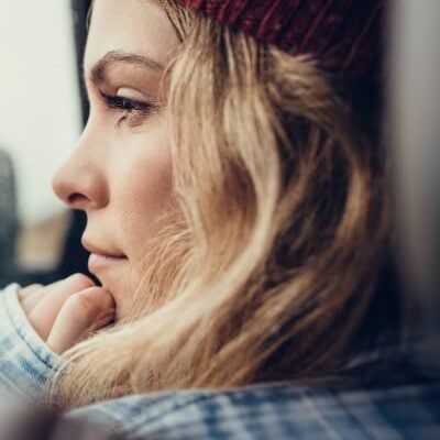 Young woman in red knit cap thinks while looking out window