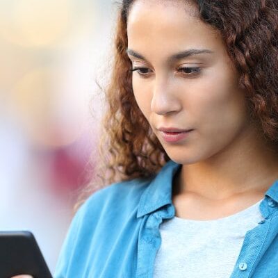 brunette in denim shirt reads cell phone screen