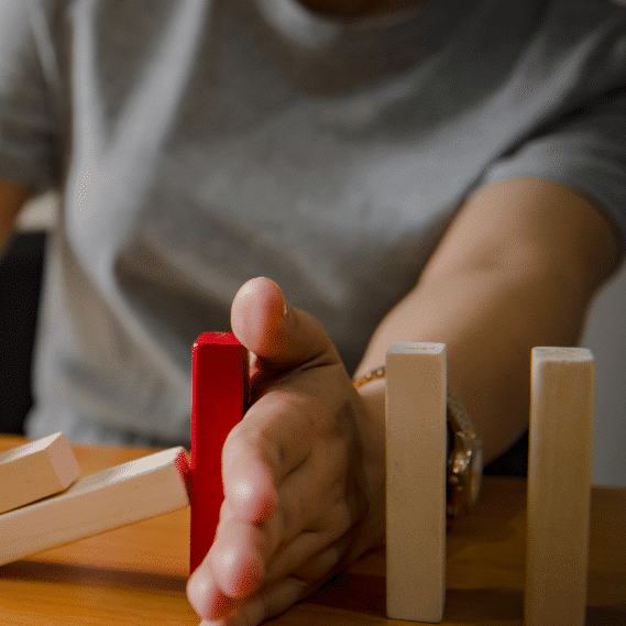 hand of person in gray shirt stops falling dominoes